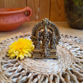 Handcrafted brass idol set featuring Lord Perumal with Sridevi and Bhudevi, displayed on a woven mat with a yellow flower and a terracotta pot in the background.