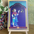 Decorative artwork of a lady admiring a parrot in a cage, framed by a minaret-style arch with intricate details, displayed on a wooden easel.