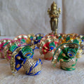 Vibrant handcrafted decorative turbans with embroidered peacock feather motifs, zari detailing, and gold accents, displayed with a brass deity statue.