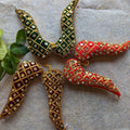 Handcrafted Vaagamalai garland in red, green, and maroon with gold latticework and mirror embellishments, placed on a textured surface with green leaves.