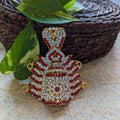 Gold-plated crown-shaped pendant with red and white stones on a woven and leafy background.