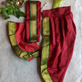 Traditional orange dhoti and angavastram set with green and gold zari borders, displayed on a textured background with leafy accents.