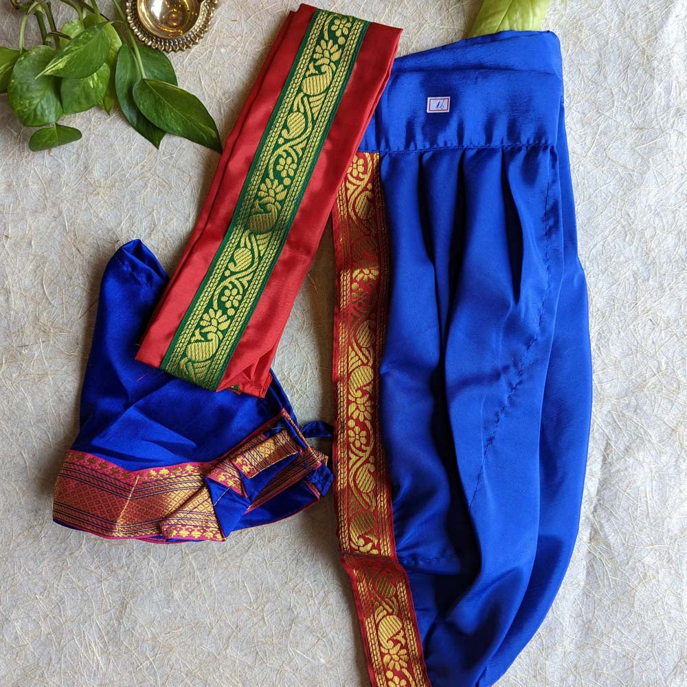 Royal blue dhoti and angavastram set with red and gold zari borders, displayed on a textured background with leafy accents.