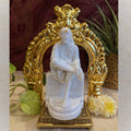 Ornate golden brass Thiruvachi with intricate carvings, placed on a tabletop surrounded by flowers and plants.