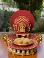 Kashi Vedi festive pooja setup — Chaturdarsh maroon backdrop, Vira Sinhasan with Banarasi fabric, Petite Gajra Toran ringed around the base, and Motirang dangler platter, styled with brass Ganpati murti for display. Handmade by IBHI.