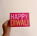 Greeting card that says Happy Diwali on bold pinkish-red background.